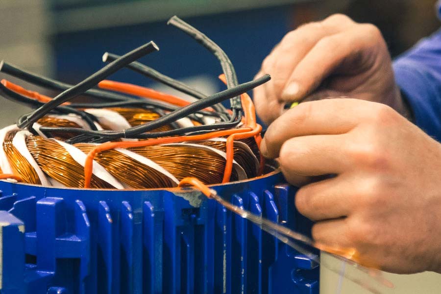 Manos de técnico rebobinando los cables de un motor eléctrico azul